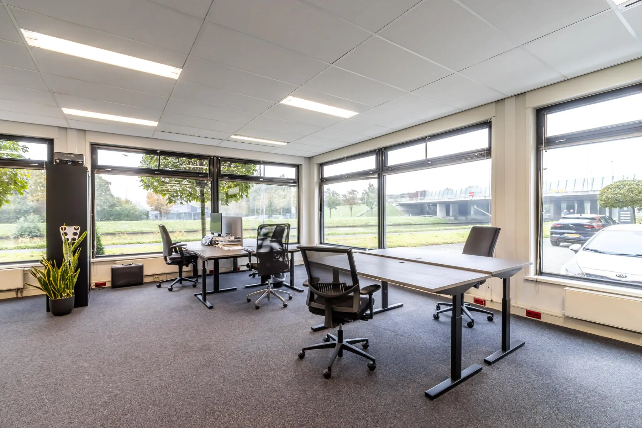 Modern ingericht kantoor aan de Lage Biezenweg met grote ramen en uitzicht op groen en een viaduct.